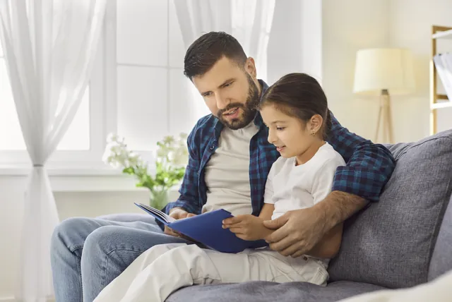 Father reading a book with his young daughter at home