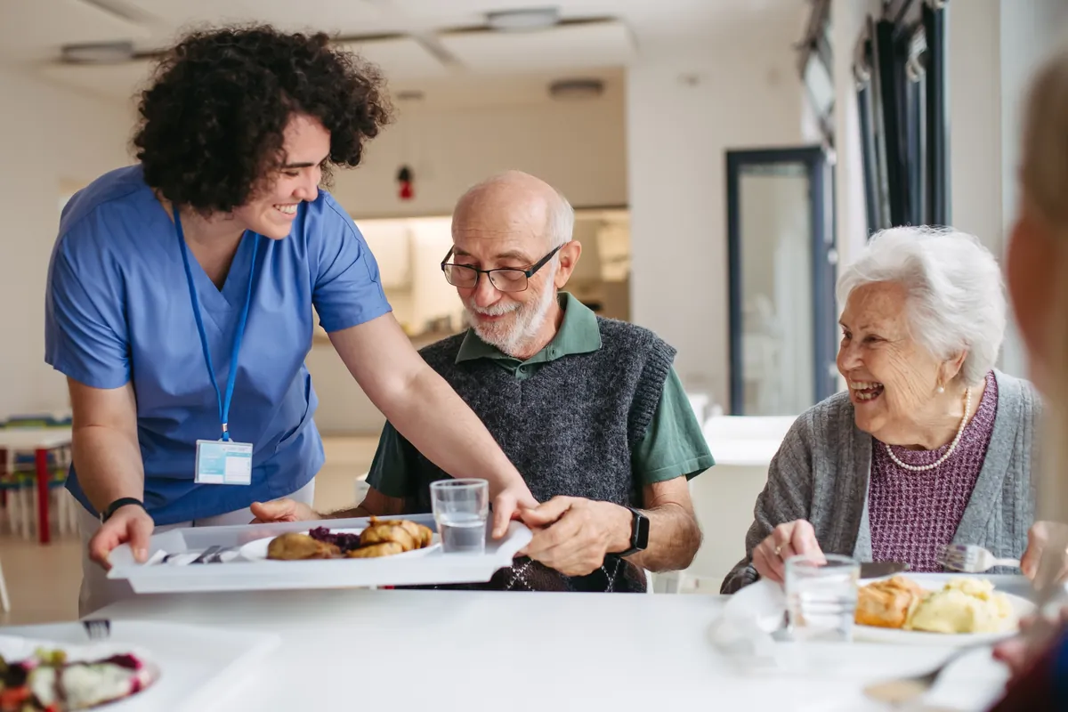 Aged care worker serving lunch to smiling residents