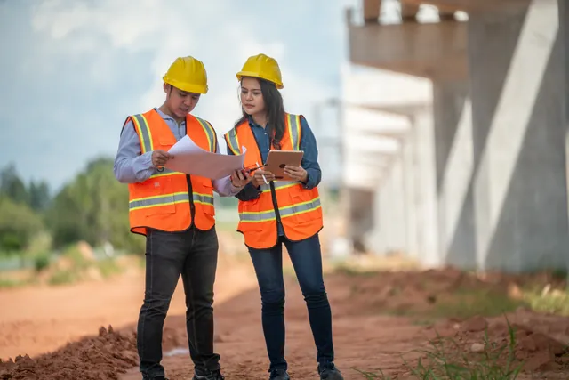 Engineers in safety gear reviewing plans on a sunny construction site