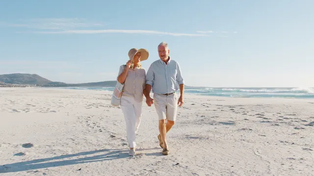 Retired couple walking together along a sunny beach